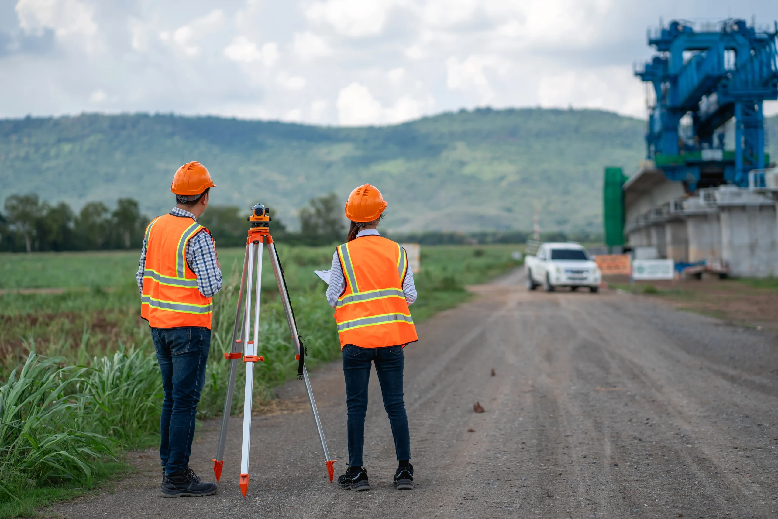 Survey team using a theodolite and construction plans for a set out survey, with civil engineers taking measurements on a road construction site.