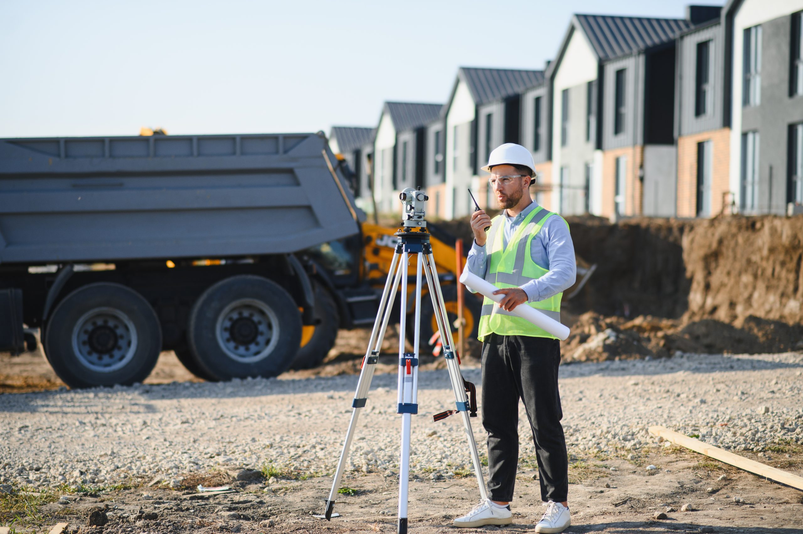 Male surveyor holding blueprints and using a walkie-talkie while supervising a new residential building site during a feature survey
